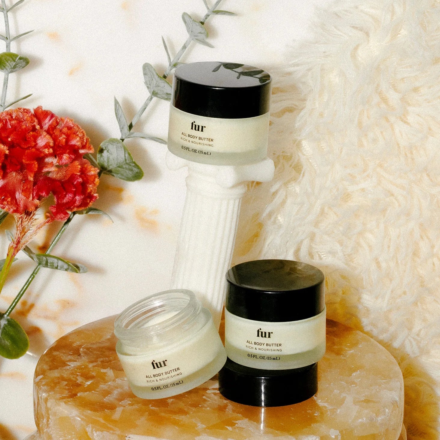 Three skincare products on a marble surface with flowers and a textured white background