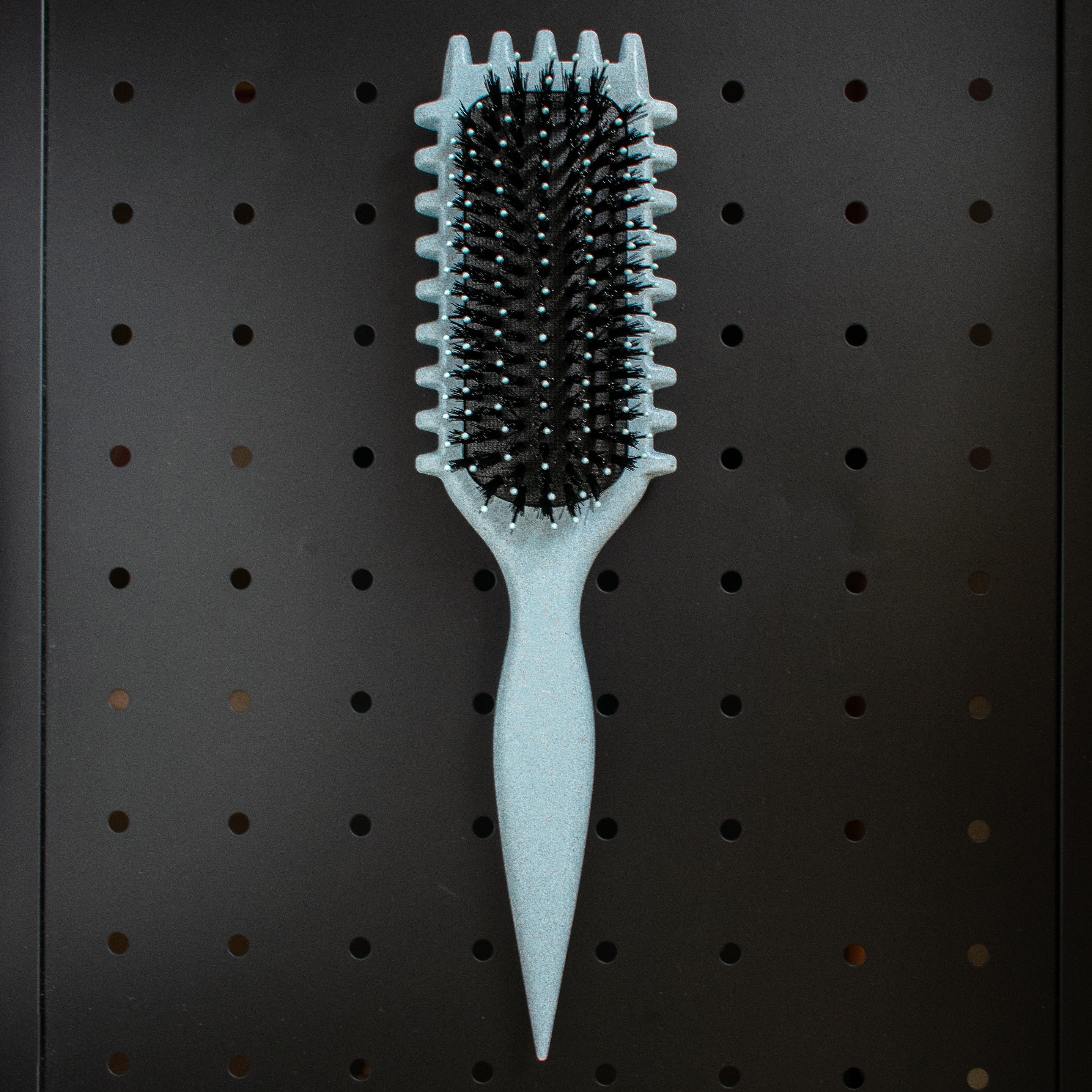 Blue curly girl hairbrush with black bristles on a pegboard background