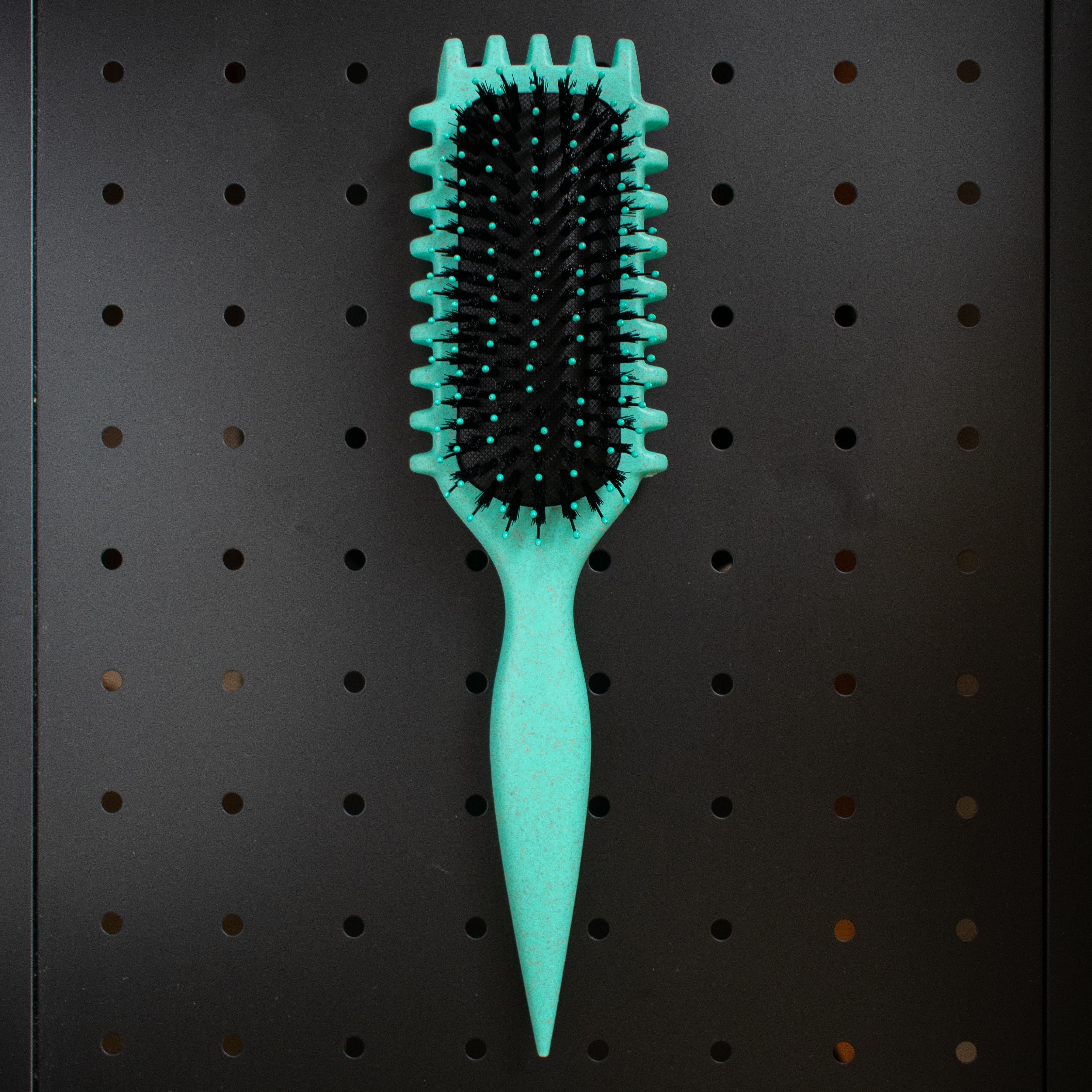 Green curly girl hairbrush with black bristles on a pegboard background