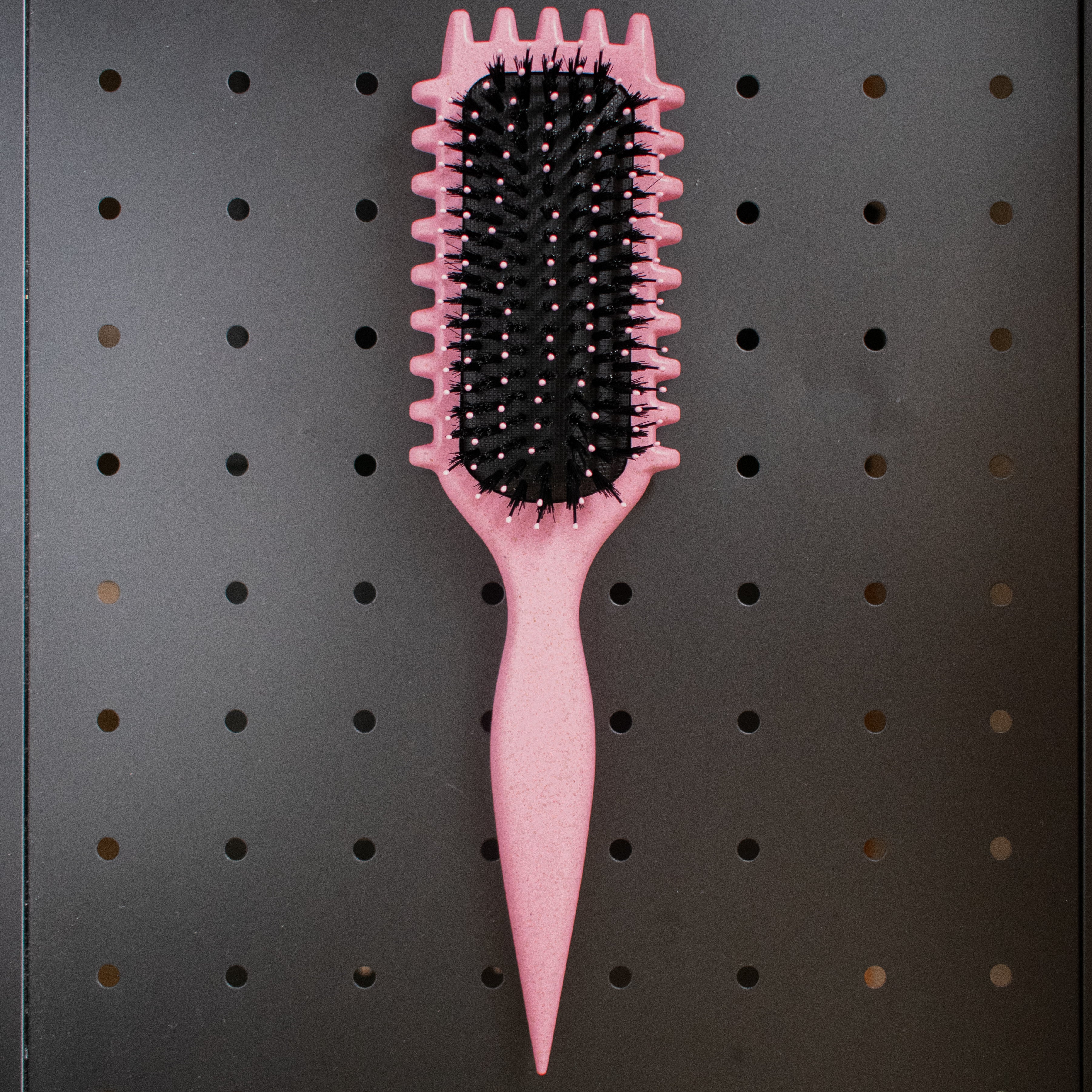 Pink curly hair hairbrush on a black pegboard background