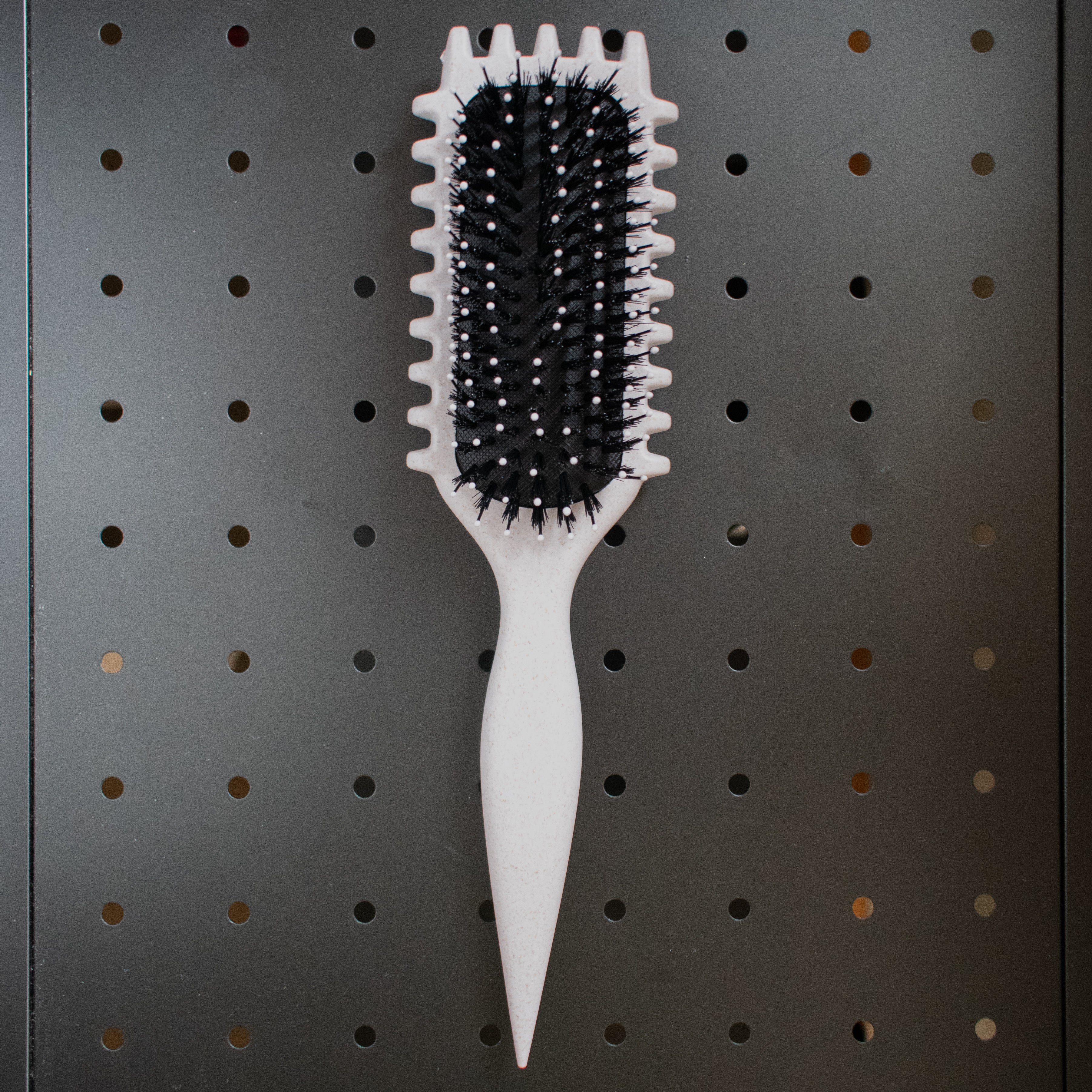 White curly girl hairbrush with black bristles on a pegboard background