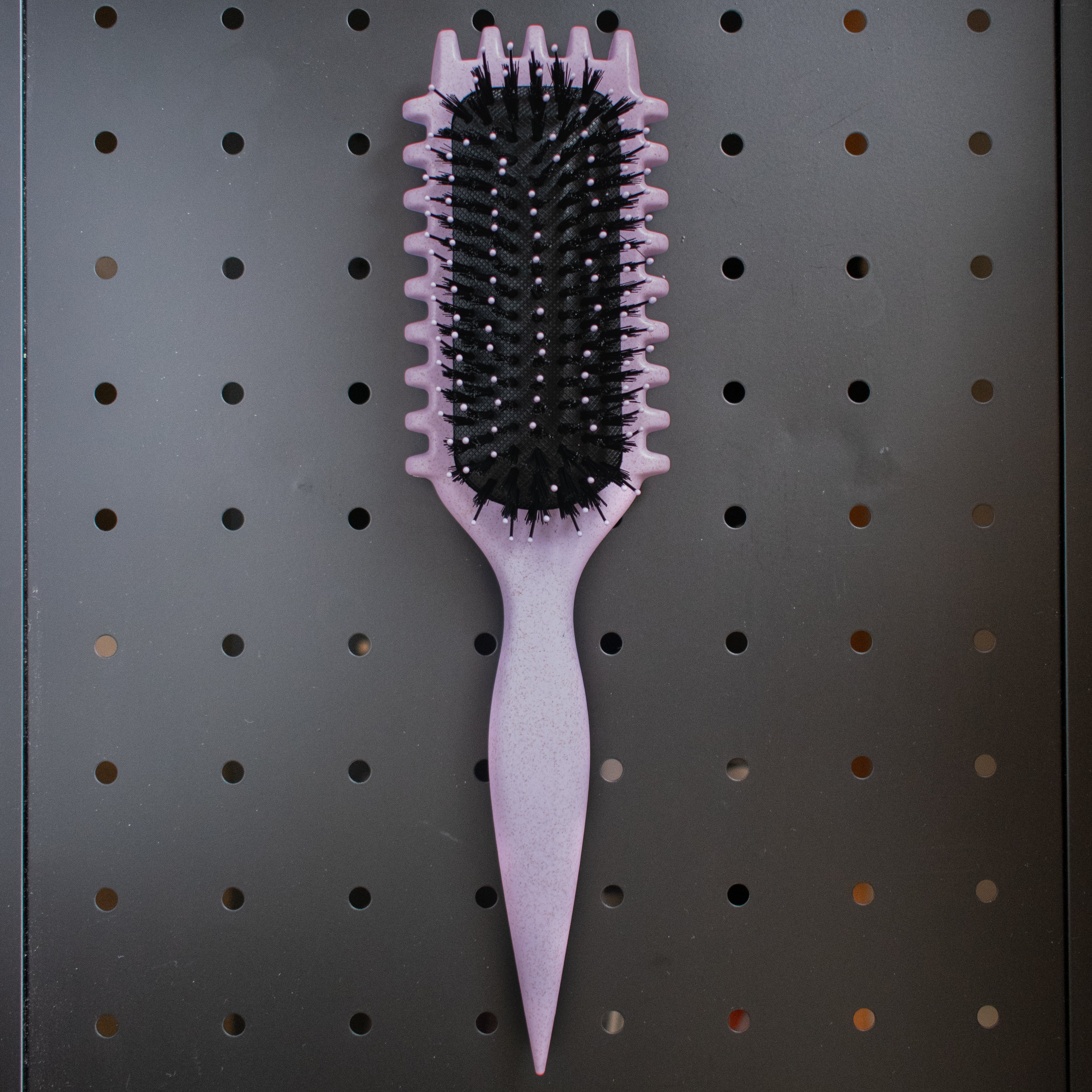 Purple curly hair hairbrush on a pegboard