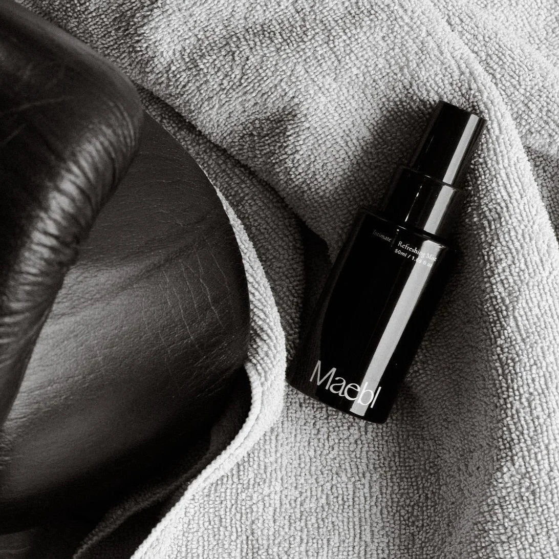 Black and white image of a bottle of Maebl Refreshing Mist on a textured surface.