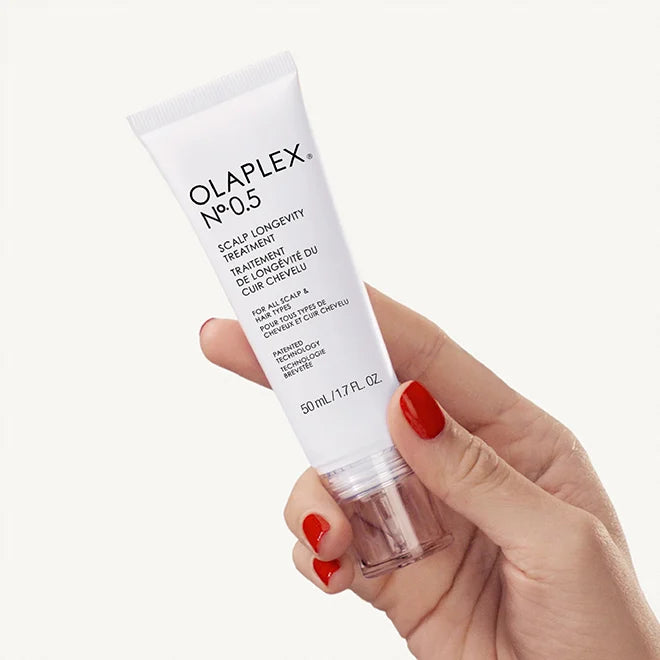Olaplex No.05 scalp longevity treatment held by a hand with red nail polish on a white background
