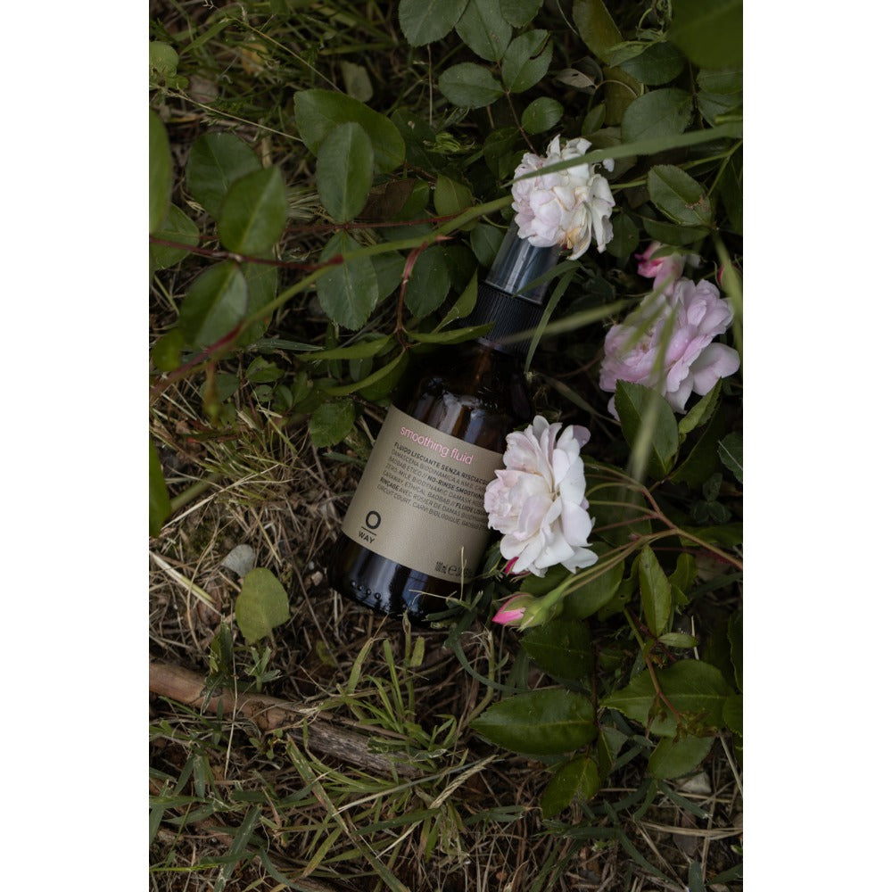 Oway Smoothing Fluid 100ml bottle amongst white blossom