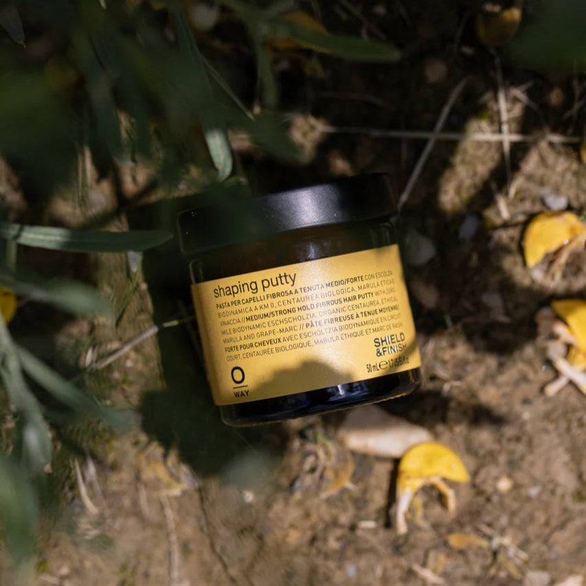 Jar of shaping putty on a natural background with leaves and dirt.