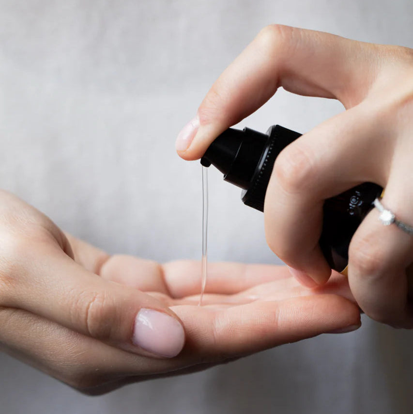 Person holding a black spray bottle over an open palm with a blurred background