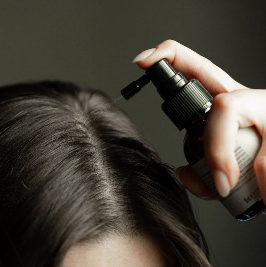 Person applying a hair product to their head using a spray bottle.