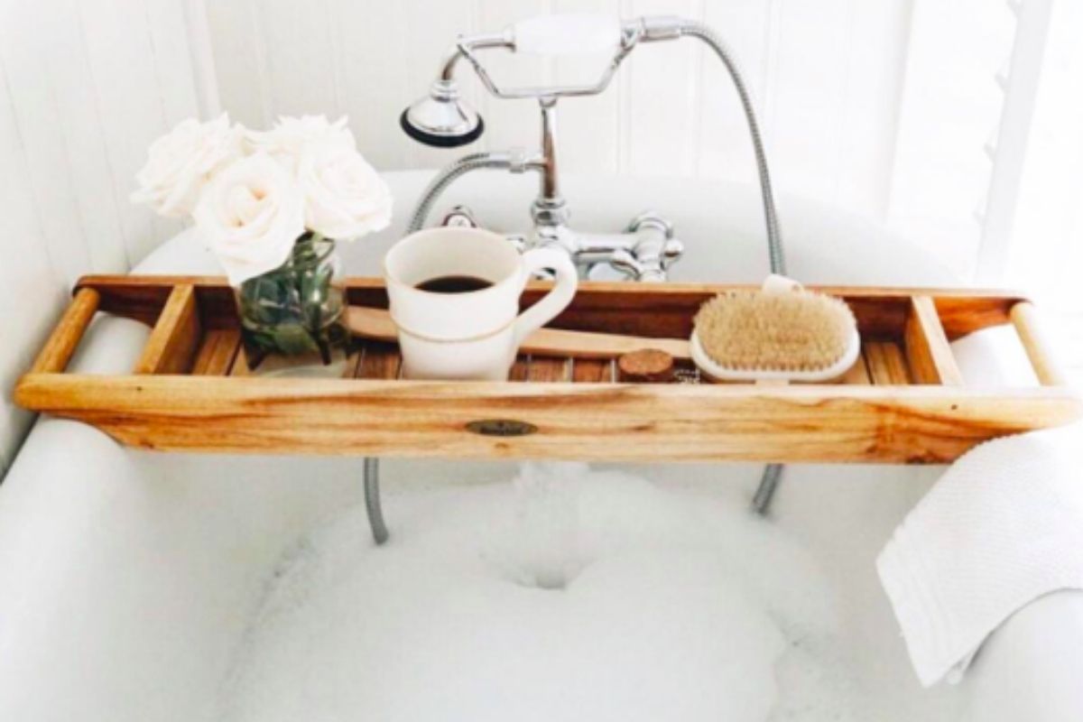 self care tips blog picture shows a cup of coffee sitting on. holder over a bubble bath with flowers and a loofer