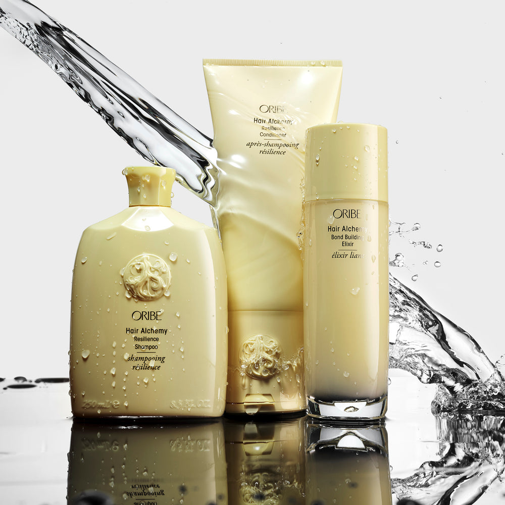 Oribe Hair Alchemy Resilience Shampoo, Conditioner and Bond Building Elixir bottles with a splash of water