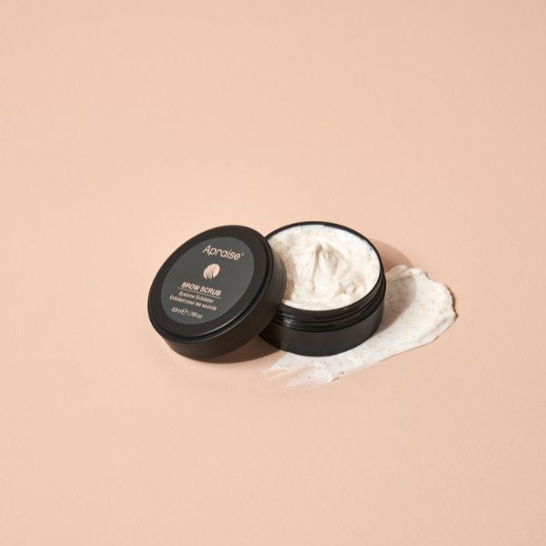 Open jar of Apraise brow exfoliating scrub on a beige background