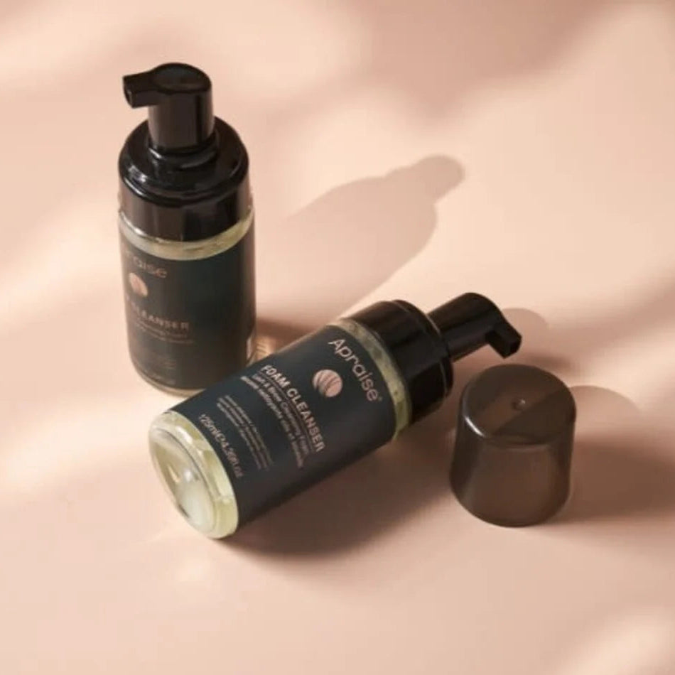 Two bottles of Apraise foam cleanser on a soft pink background