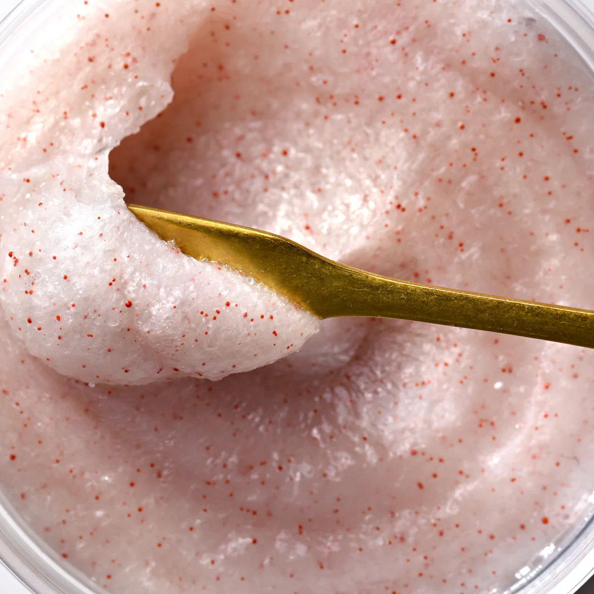 Pink scrub with red specks and a gold spoon in a clear container
