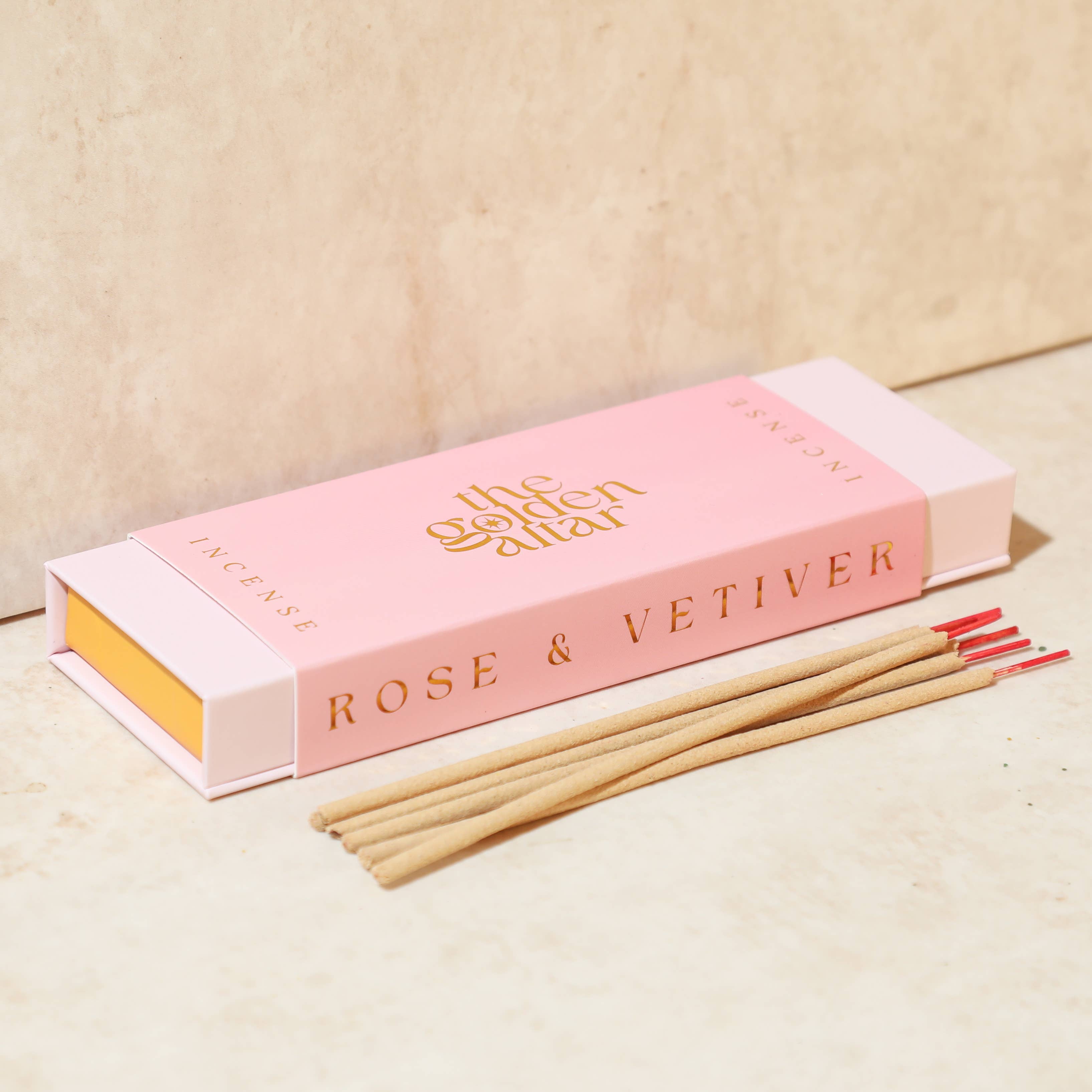 Incense sticks with a pink box labeled The Golden Altar with the scent 'Rose & Vetiver' on a beige background