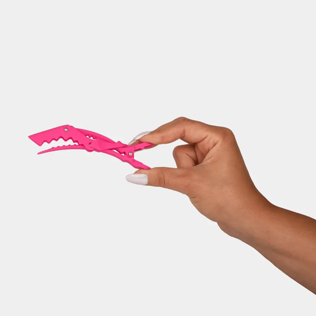 Hand holding a pink hair clip against a white background