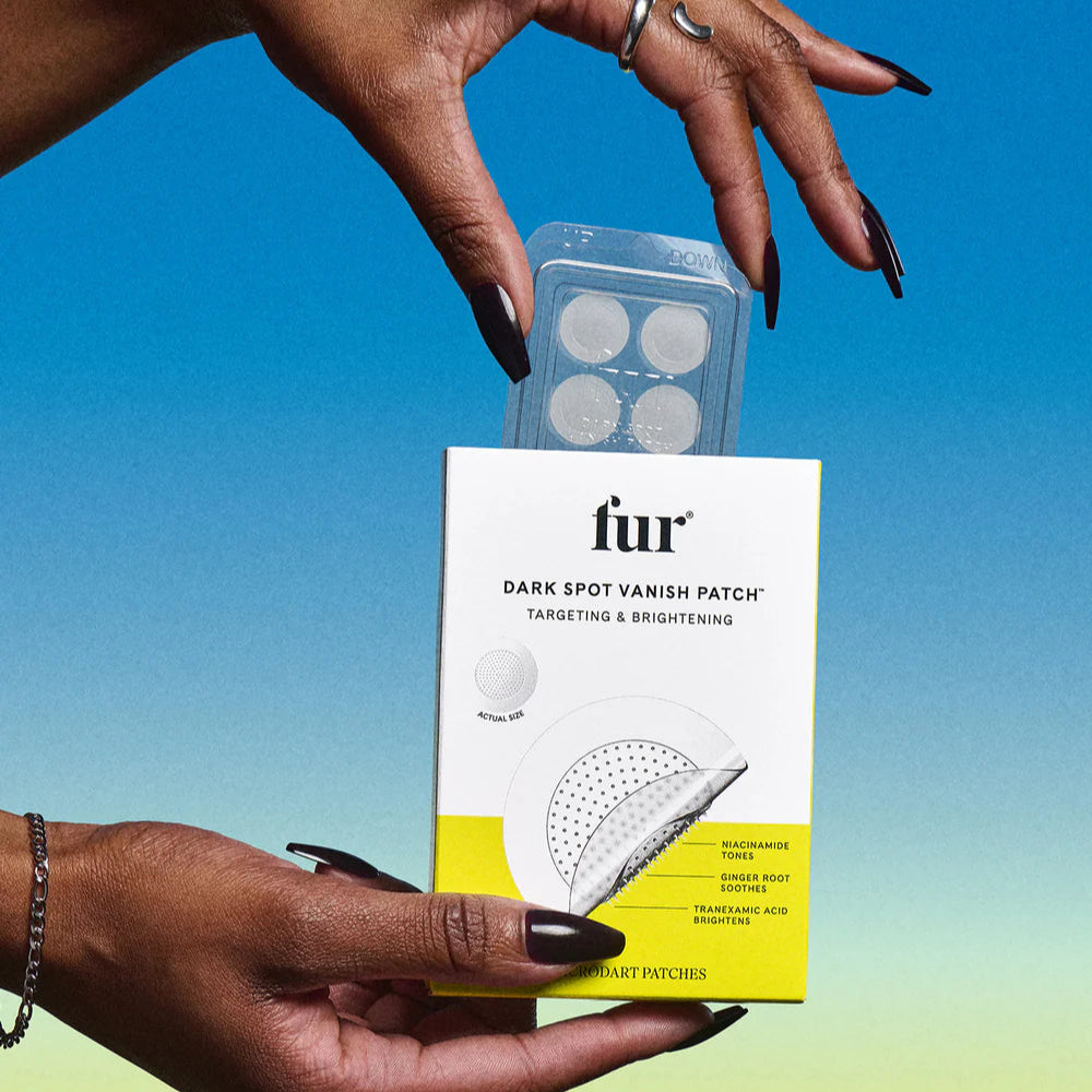 Hands holding a box of fur Dark Spot Vanish Patch against a gradient blue to yellow background