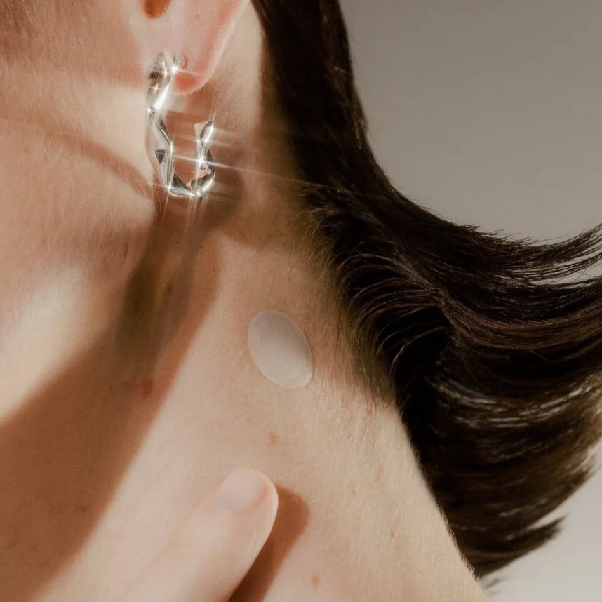 Close-up of a person wearing a silver hoop earring with a neutral background