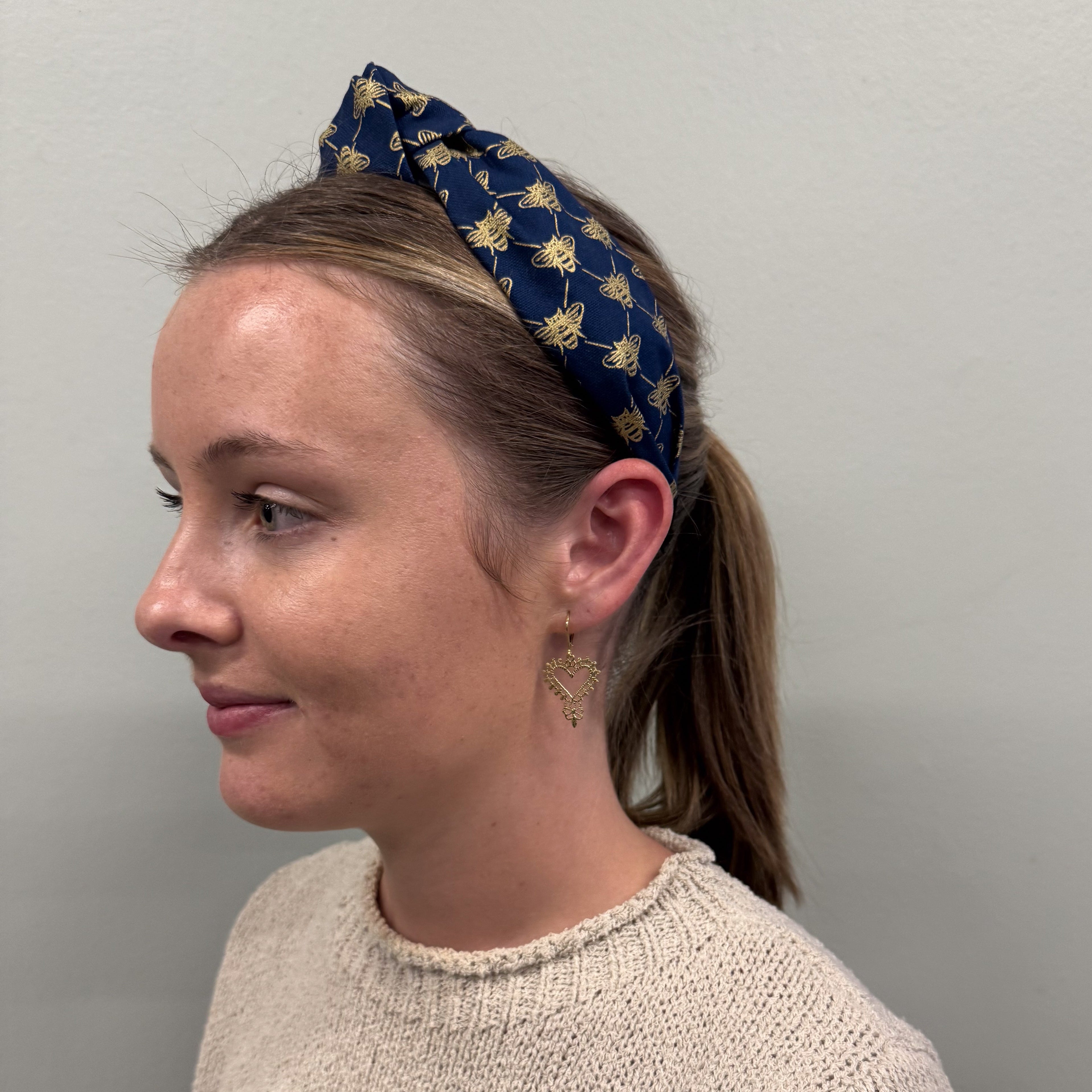 Woman wearing a blue headband with gold bee patterns against a plain background