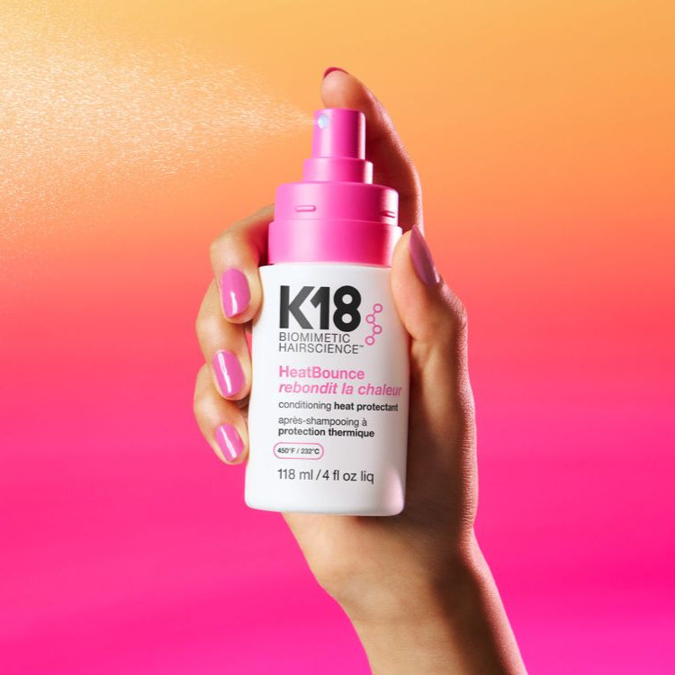 Hand holding a K18 hair care product against a colorful gradient background