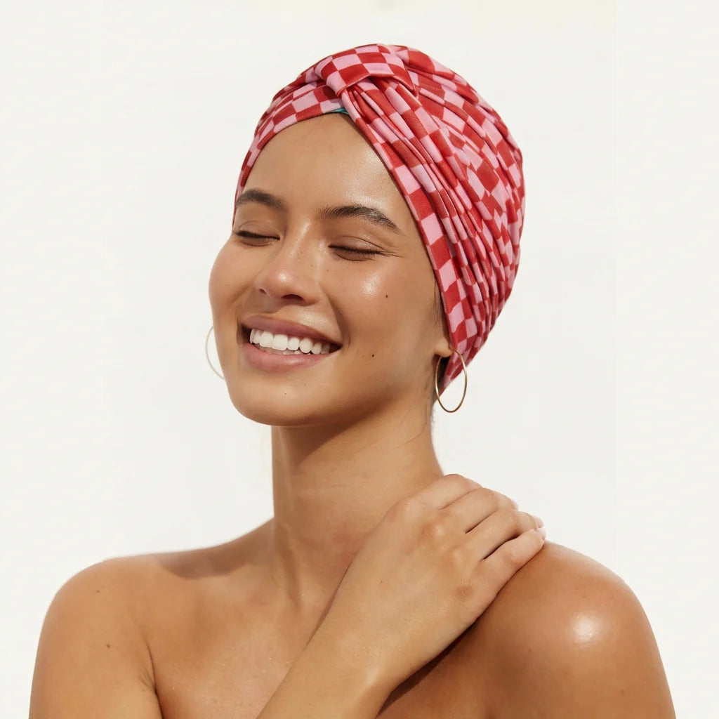 Woman wearing a red and white checkered Louvelle Shower Cap on a plain background