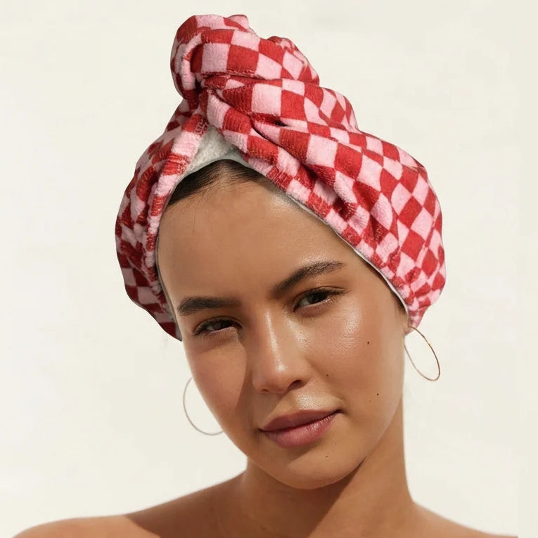 Woman wearing a red and white checkered towel wrap from Louvelle on her head against a beige background