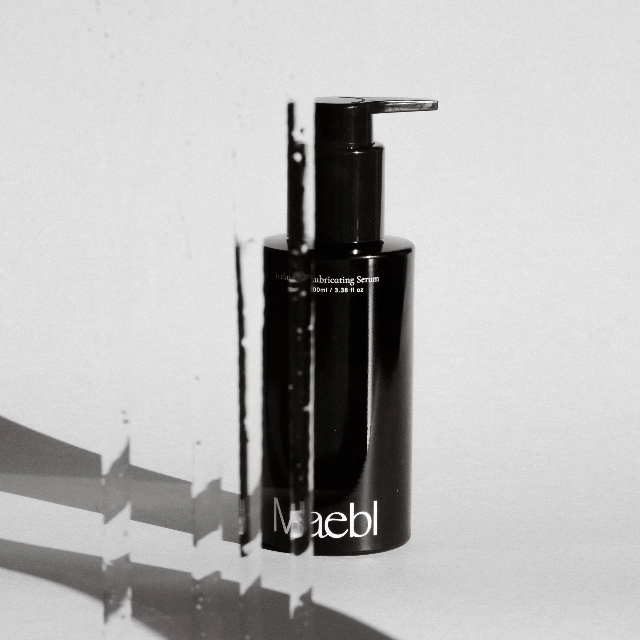 Black bottle of Maebl Intimate Lubricating Serum with pump on a reflective surface