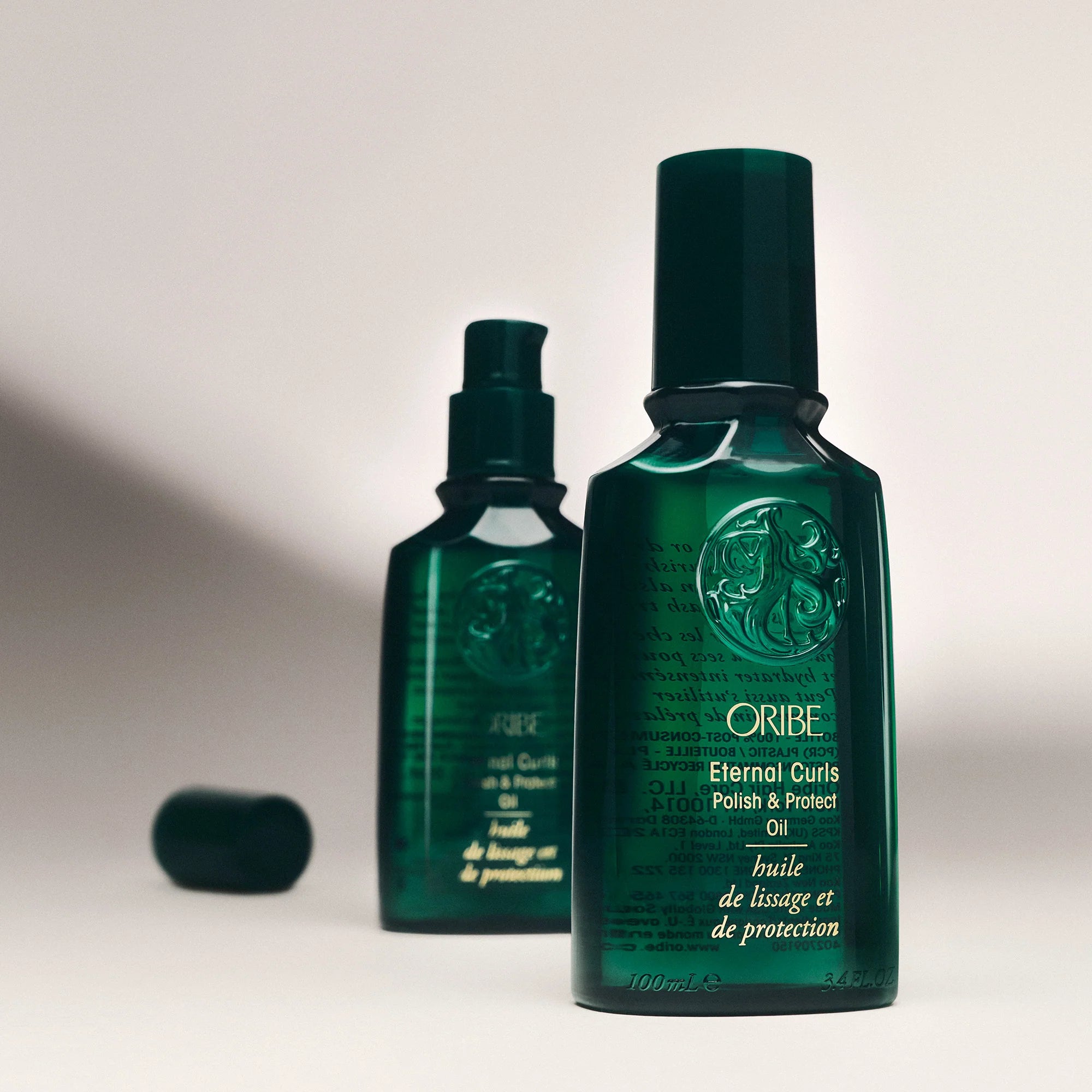 Two green bottles of Oribe Eternal Curls Polish and Protect Oil on a light gray background