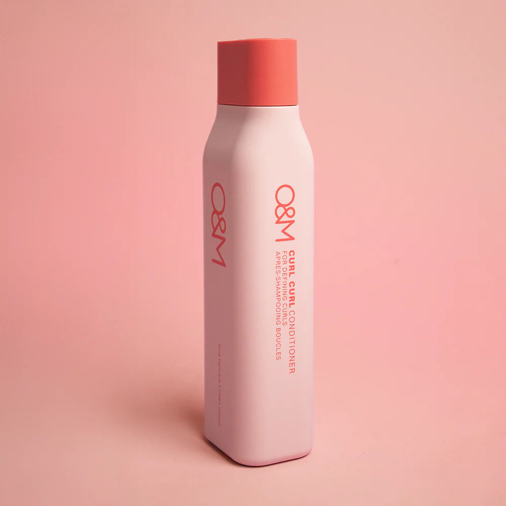 O&M Curl Curl Conditioner bottle of hair conditioner on a pink background