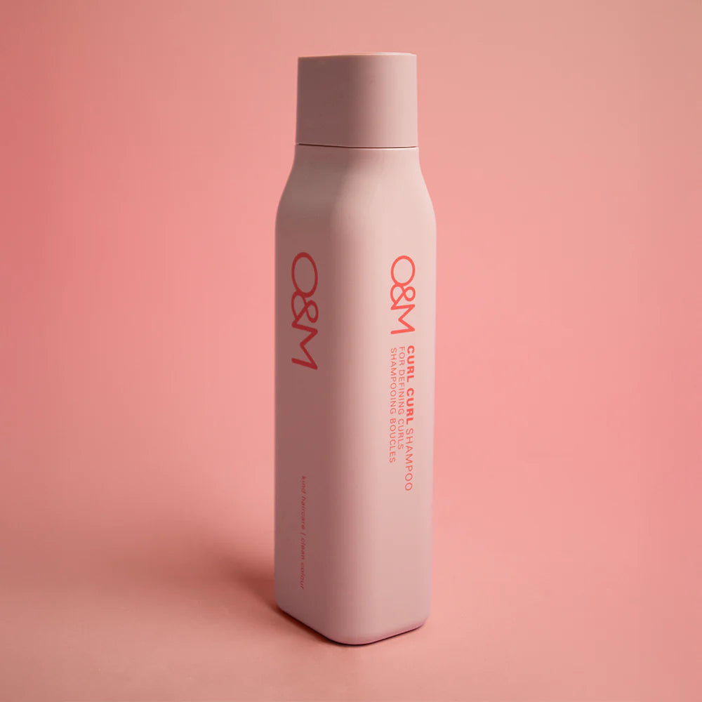 Pink bottle with red text "O&M Curl Curl Shampoo' on a pink background