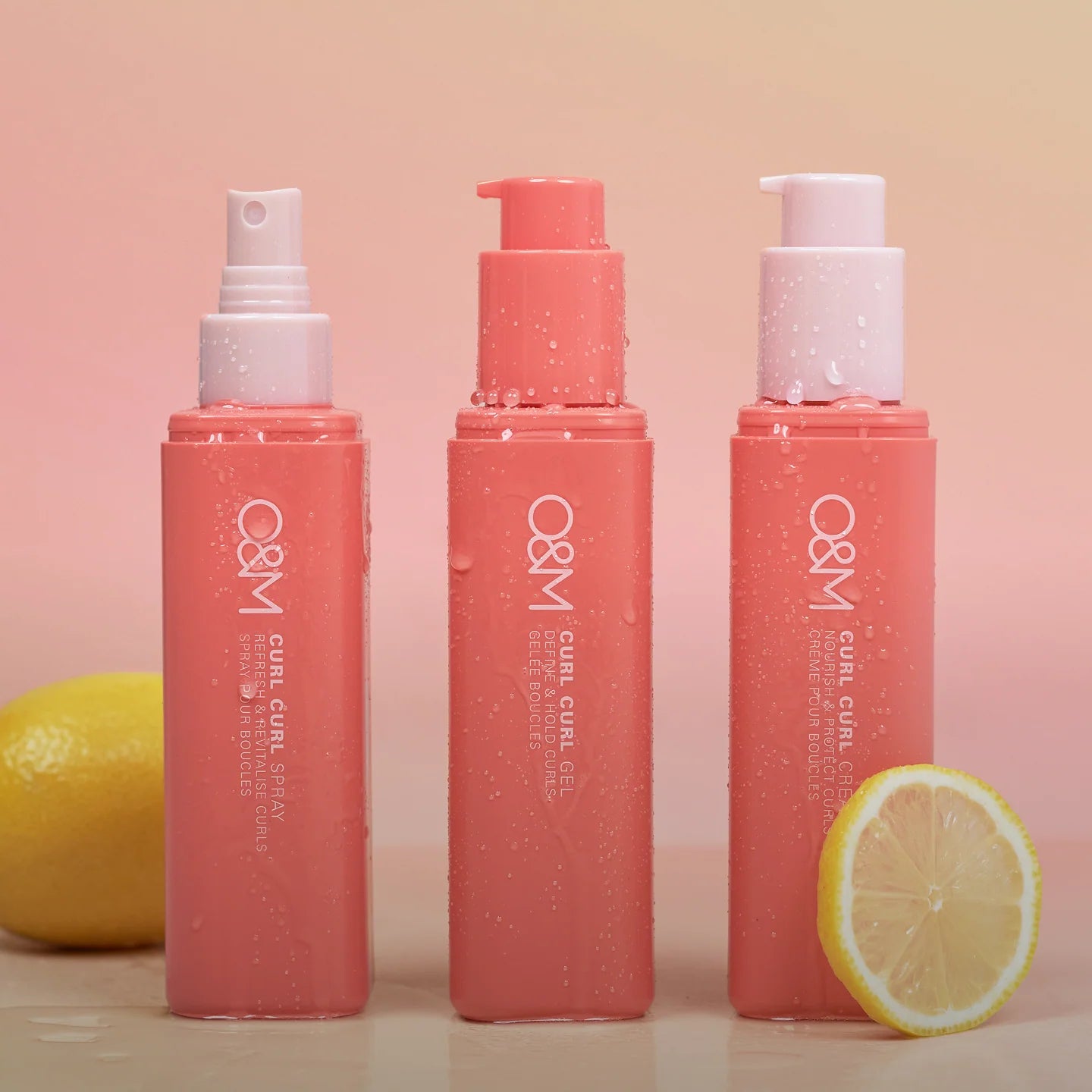Three bottles of O&M Curl Curl hair care products with lemons on a pink background
