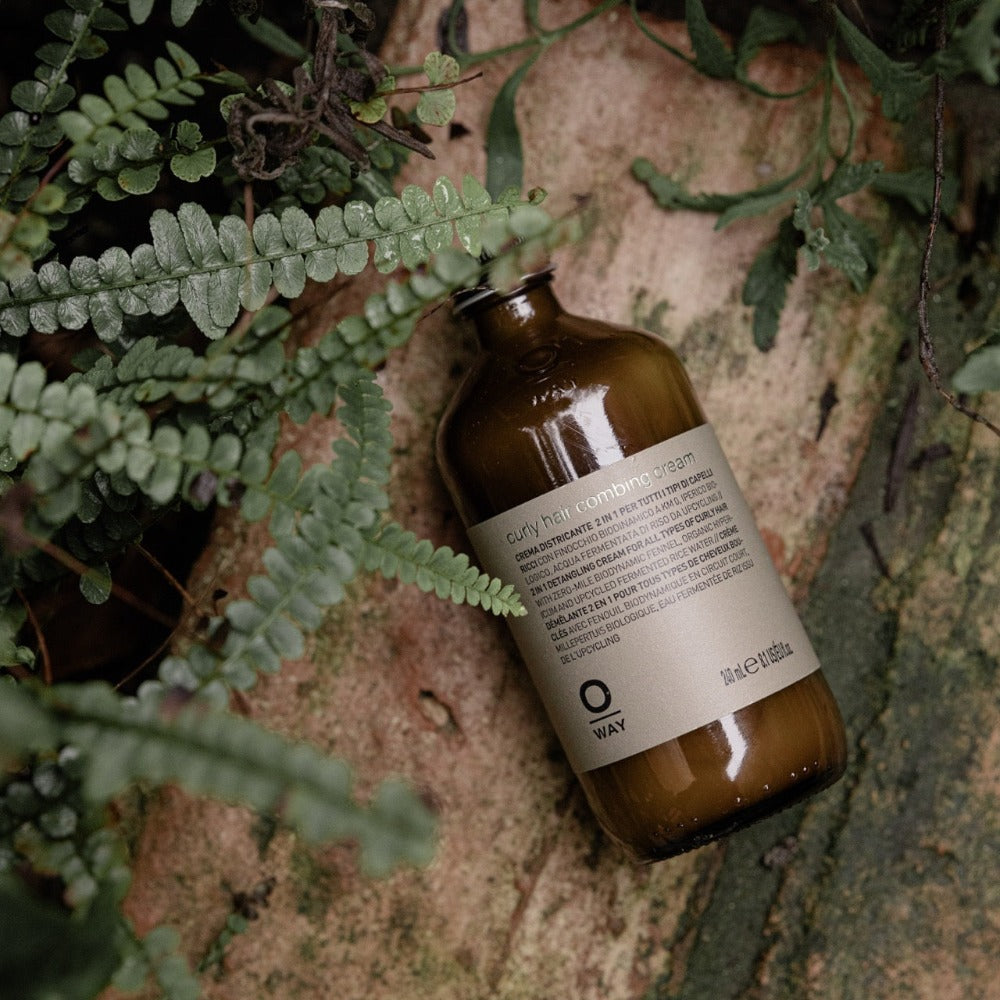 Oway Curly Hair Combing Cream bottle among plants