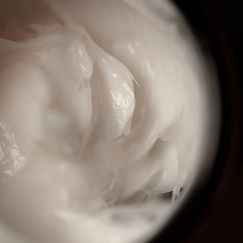 Close-up of a white cream or lotion in a container with a dark background