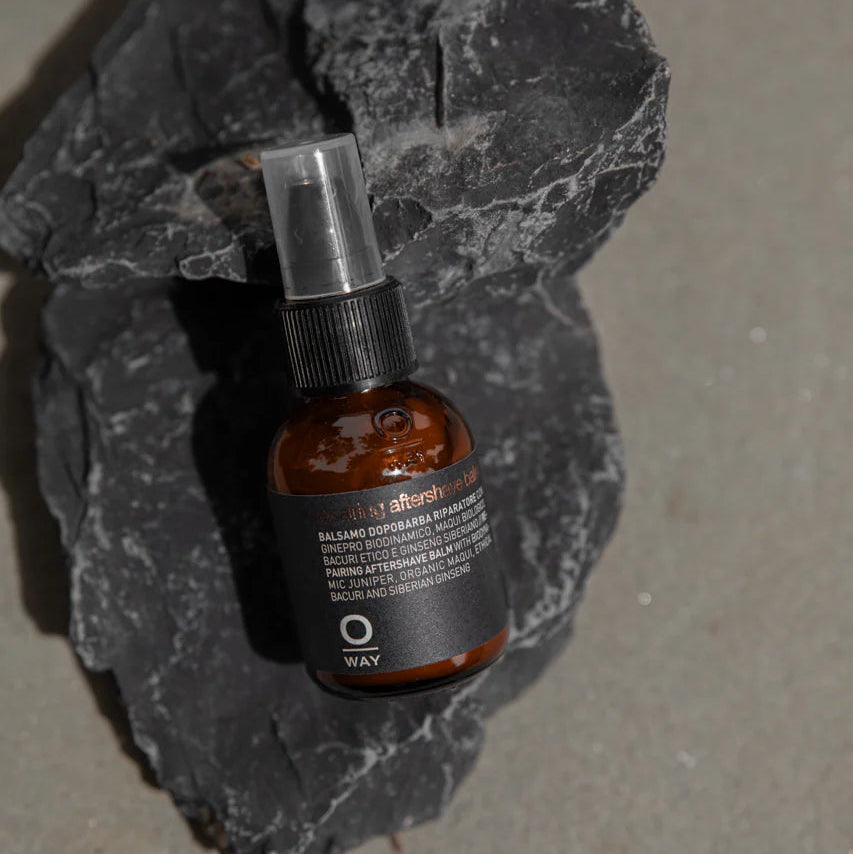 Brown bottle of Oway Repairing Aftershave Balm on a dark gray stone surface