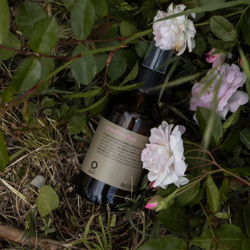 Bottle of Oway Smoothing Fluid on grass and flowers