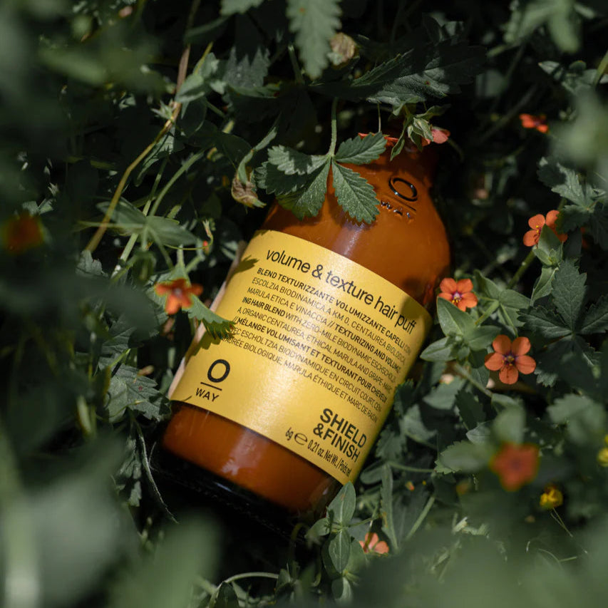 Bottle of hair product surrounded by green leaves and flowers