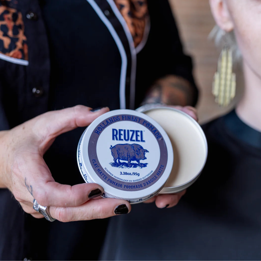 Person holding two containers of Reuzel Clay Matte Pomade with a blurred background