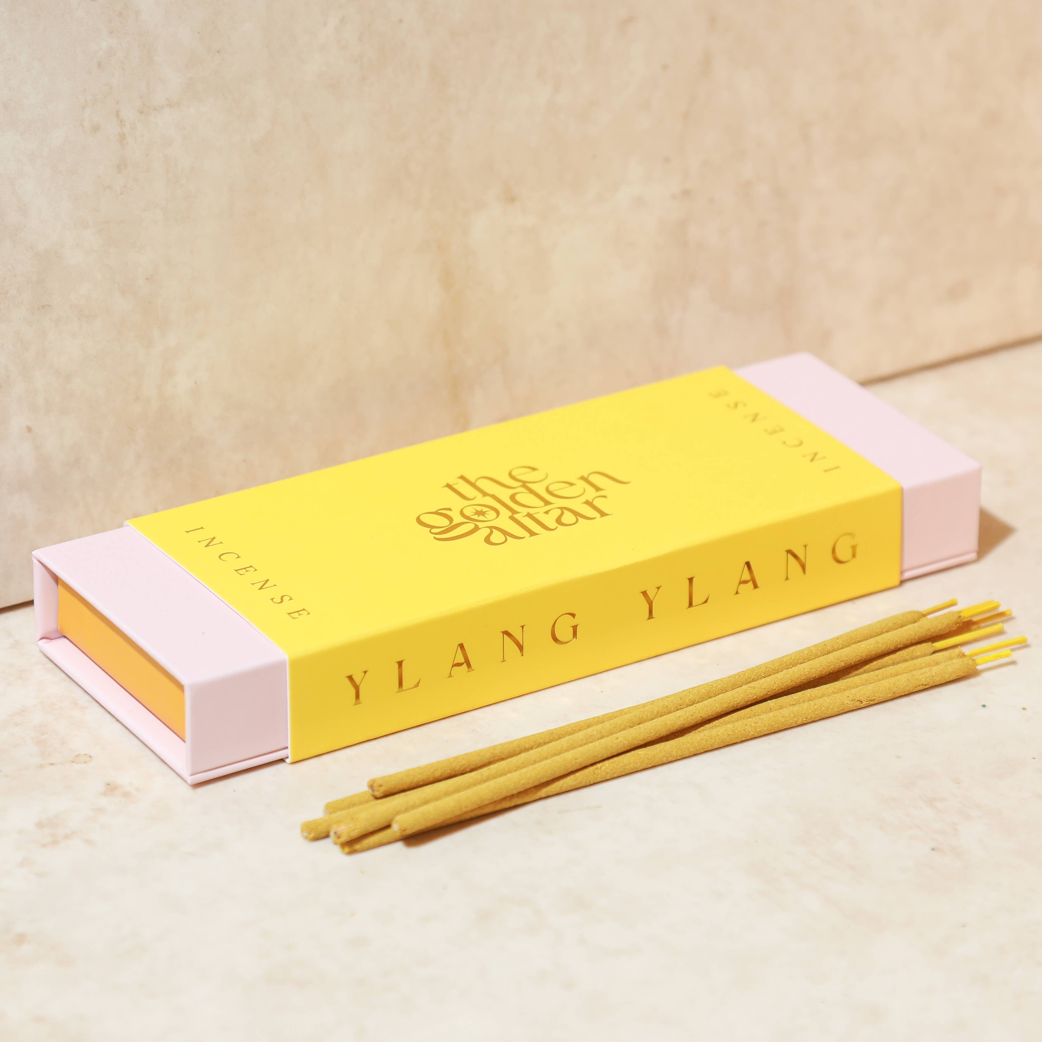 The Golden Altar Ylang Ylang incense sticks in a yellow and pink box on a beige background