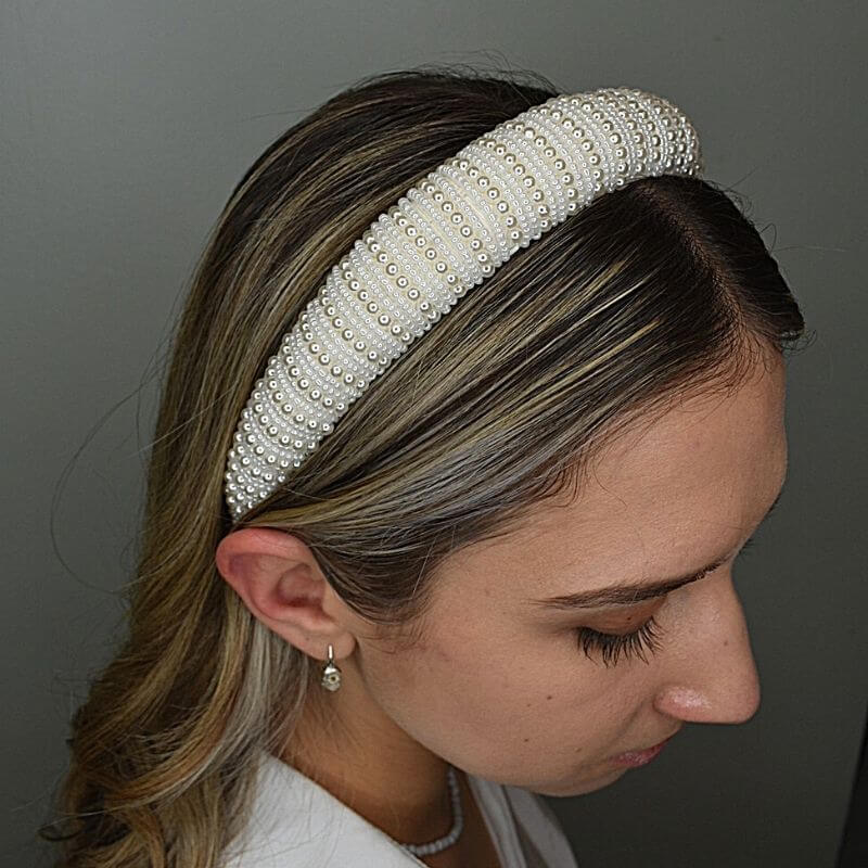 Model wears white pearl headband with small and large pearls alternating. Pearls have been strung width ways across the headband - from back to front of head. 